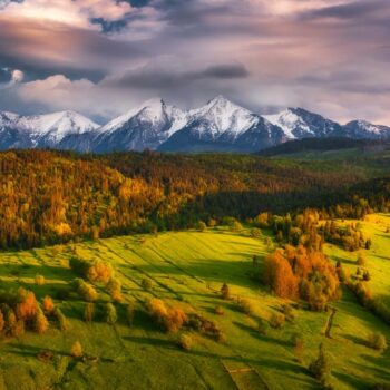 Green spring meadow with snowy mountains in the backgroound and colorful sky. High Tatras NP, Slovakia. Vysoke tatry. Osturna village
