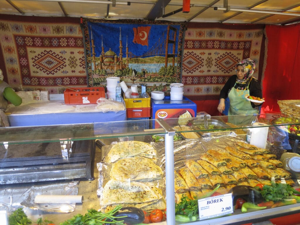 An Armenian woman standing behind a counter full of food.