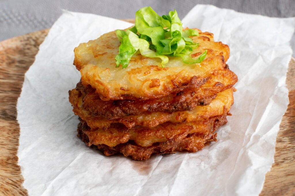 Potato pancakes, draniki, deruny, potato latkes, latkas, irish cakes, raggmunk or boxties on wood plate. Fried grated vegetable pancakes or potato fritter with onion on rustic background