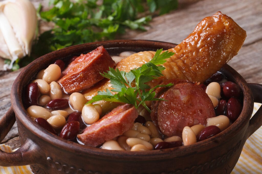 red and white beans with chicken legs and grilled sausages in a bowl on the table. close up horizontal