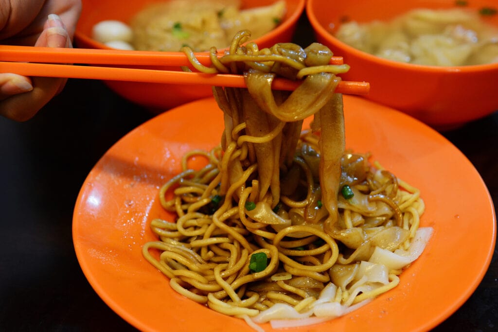 Hand with Chinese chopsticks eating Dried wonton noodles, Char Kuey Teow is a popular noodle dish in Malaysia