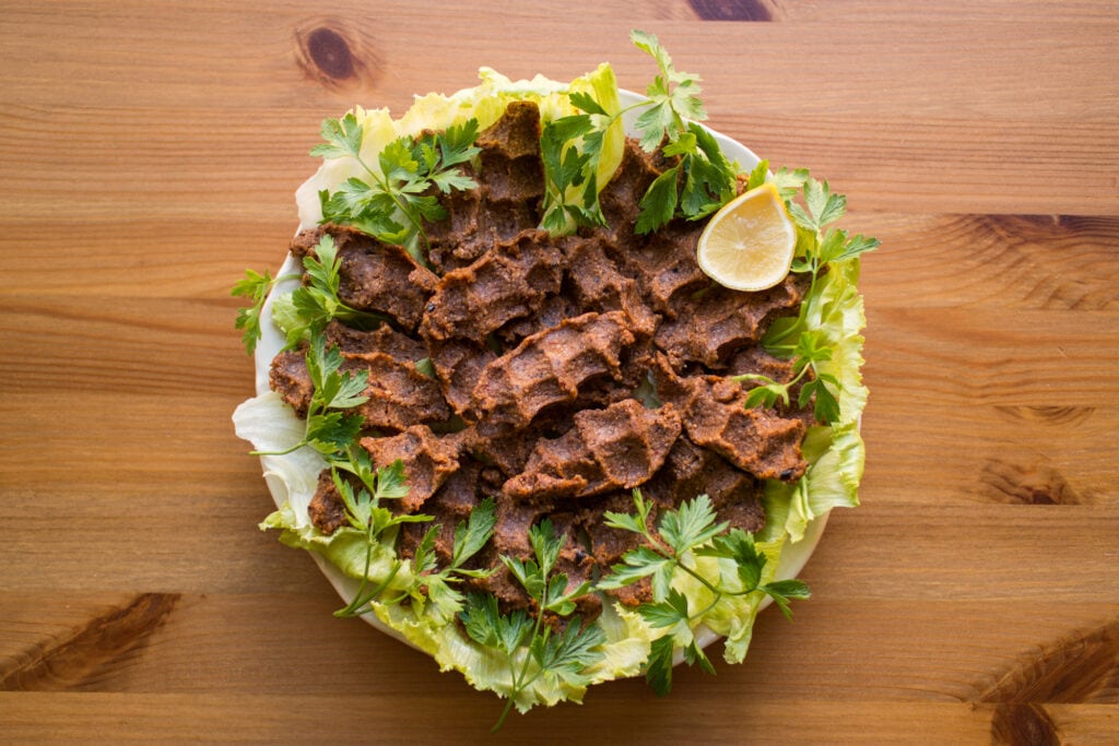 A plate of armenian food with meat and lettuce on a wooden table.