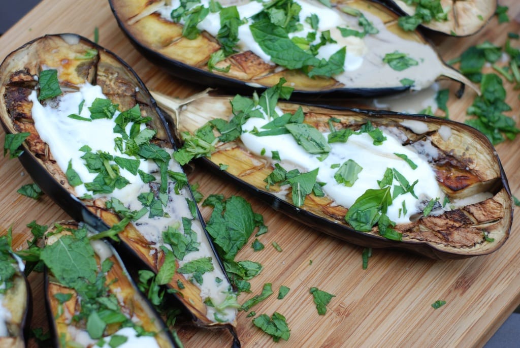 Armenian stuffed eggplants with sour cream and herbs on a wooden cutting board.