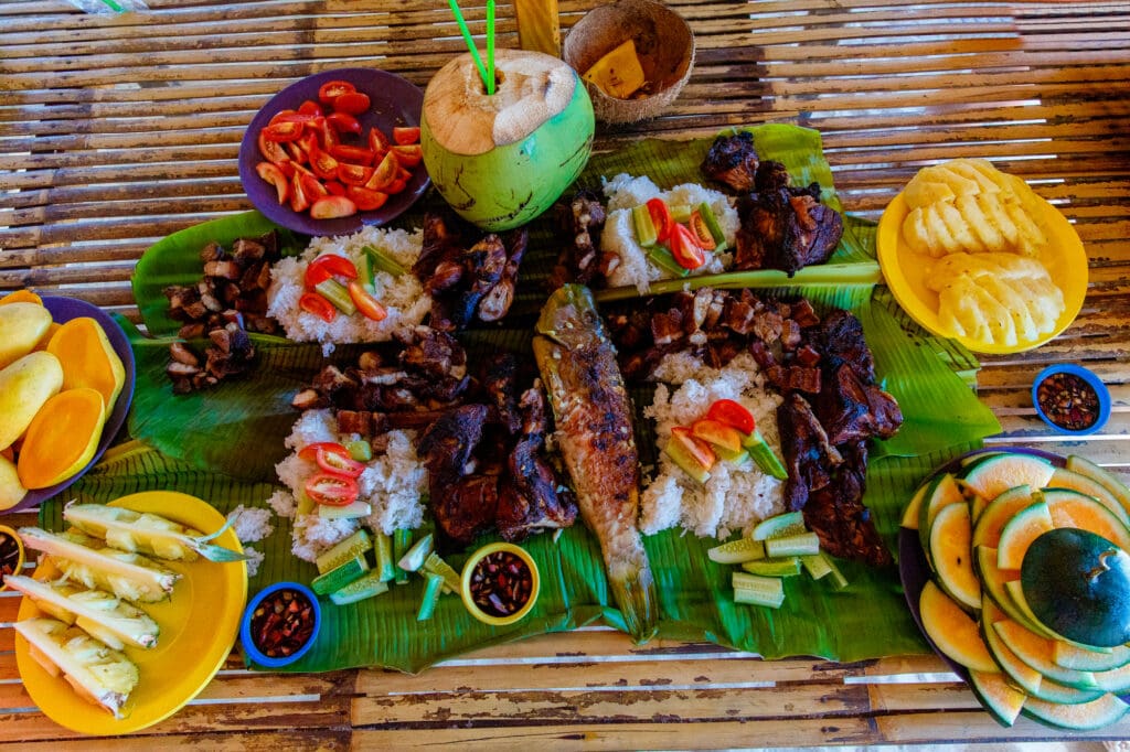 Barbecue of chicken, pork and fish is served on bamboo leaves with vegetables and fruits. 