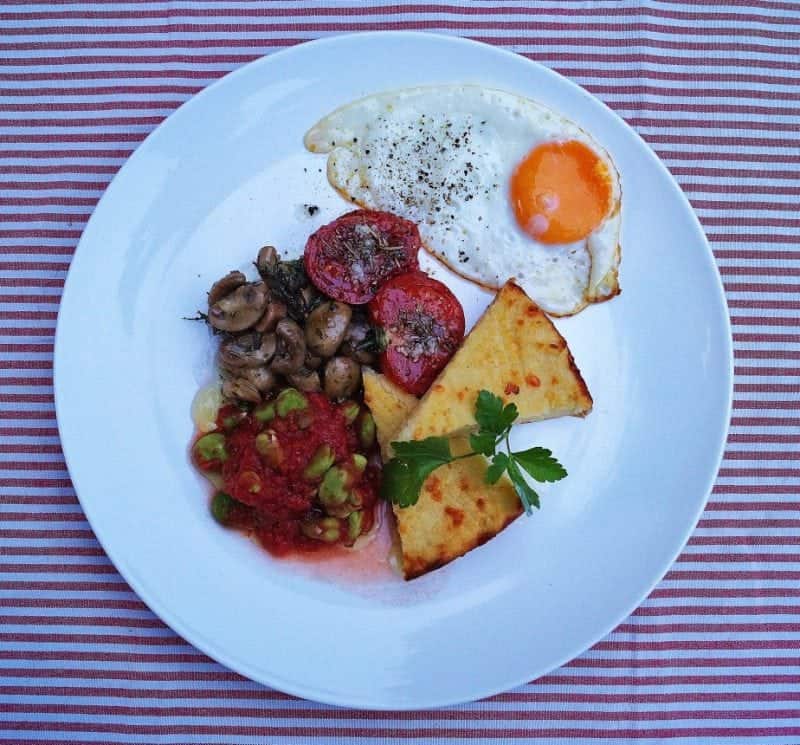 An Irish potato cake, known as boxty, topped with a fried egg, sliced tomatoes, and served alongside toasted bread.