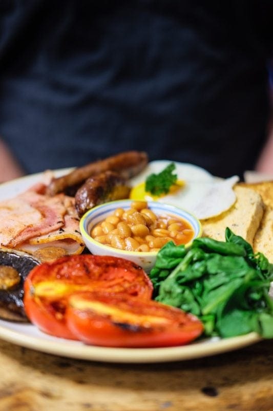 man sitting in front of a plate of a traditional Irish breakfast. The breakfast consists of fried eggs, sausages, beans, Irish bacon, mushrooms and boxty.