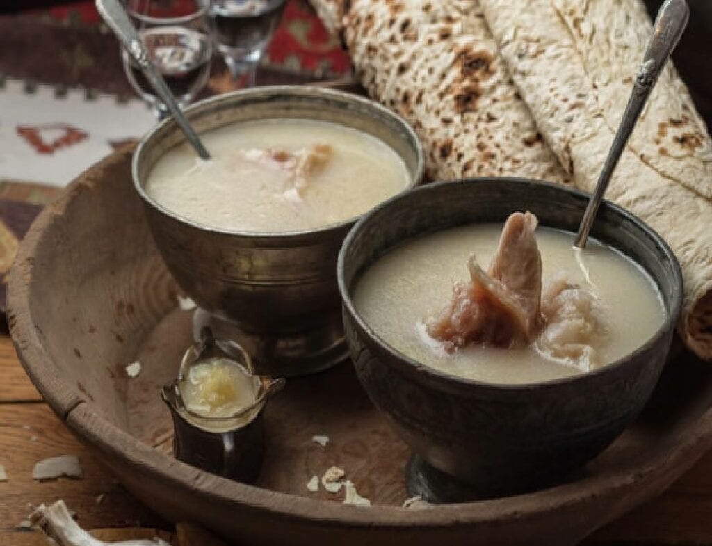 Two bowls of armenian soup and bread on a wooden table.