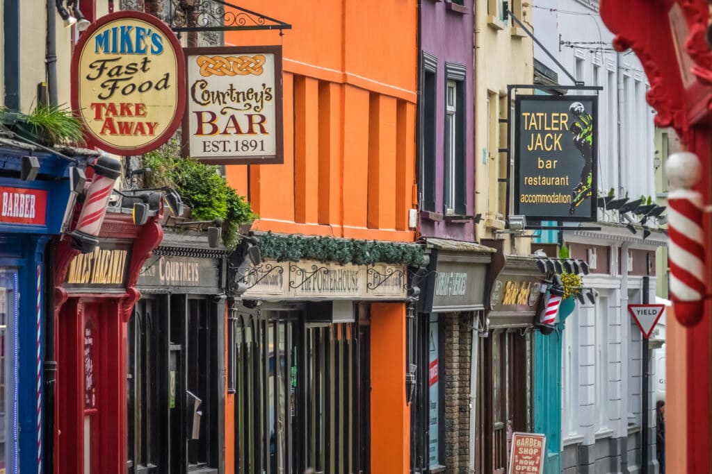 Pubs and restaurant row in Killarney Ireland. The buildings are all attached and painted with bright colours from orange to purple. The shop fronts dates back to Victorian times.
