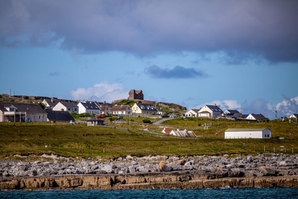 Beautiful view of the Inis Oirr island with its houses and the ruined 15th-century castle tower in a prehistoric stone fort in the background, wonderful sunny day in Aran Islands, Ireland