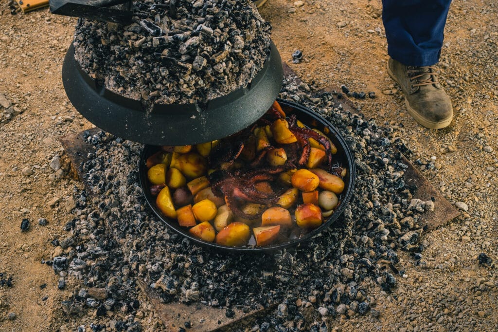 Cooking traditional balkan turkish bosnian dalmatian meal Peka in metal pots called sac sach or sache. Detail of squid or octopus with potatoes under Sache. Sac is covered with hot charcoal.