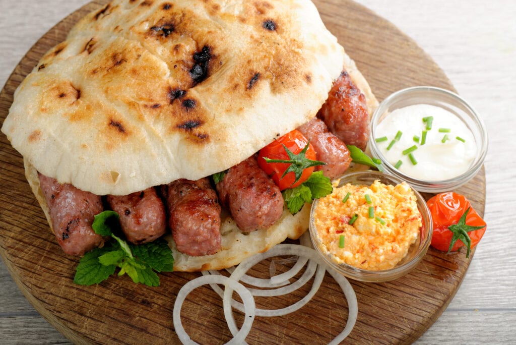 Cevapcici, a small skinless sausage cooked on the barbecue and served with: Lepinja bread, pickled red capsicum and Kajmak cheese. This dish is popular all over the Balkans, with tourists and locals.