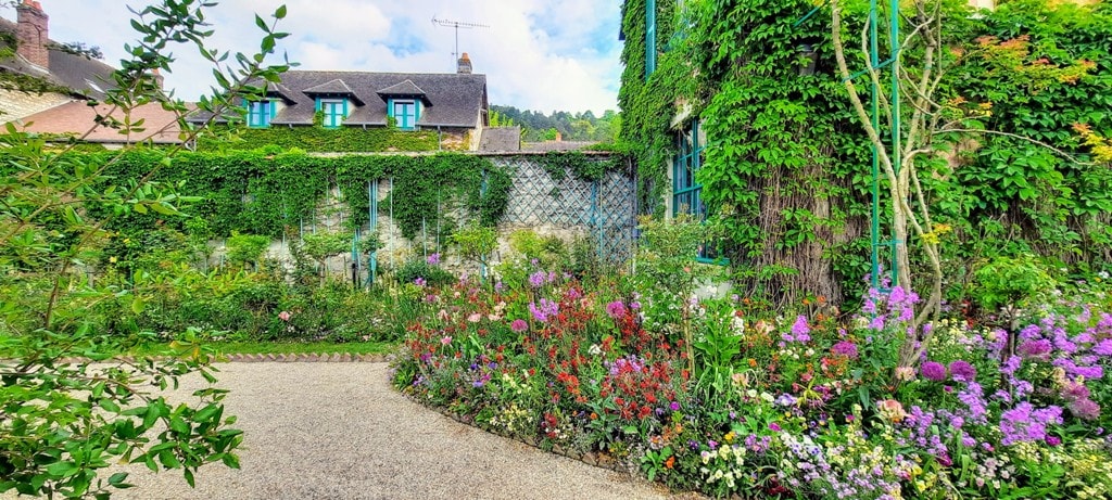 the side garden at Monet's house in Normandy the stone wall is covered in climbing vines and the gravel paths have riotous colourful flower beds beside them