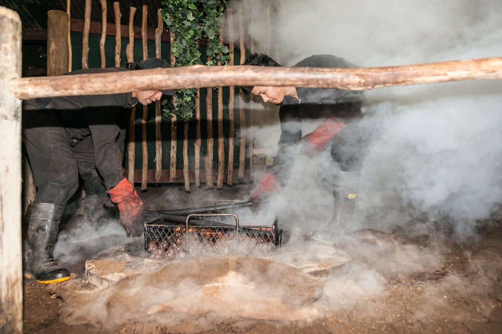 Rotorua New Zealand - April 2014; Smoke and dust fly as food is being prepared for a traditional maori feast or Hangi, by steaming through heat from underground thermal activity or heated stones in base of pit