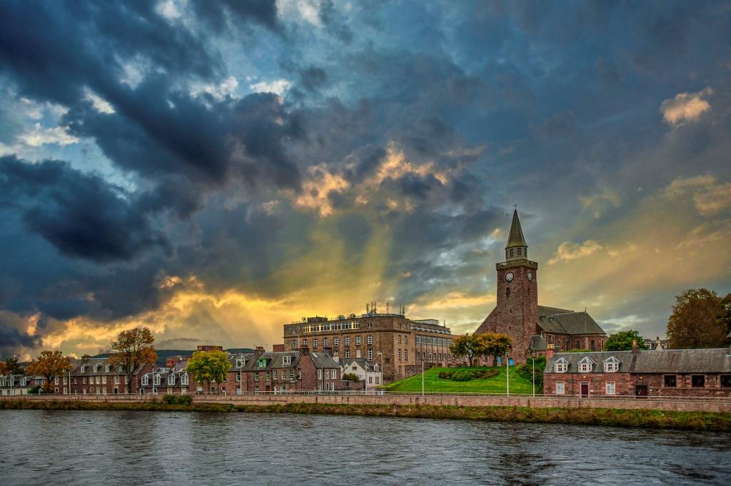 Things to do in Inverness, Scotland a gorgeous view of Inverness across the river, the sky is dark and cloudy with the sun breaking through into golden rays of light.