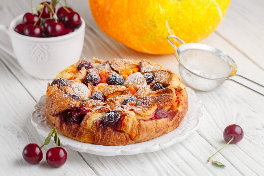 Great British Desserts bread and butter pudding on a white plate stuffed with cherries.