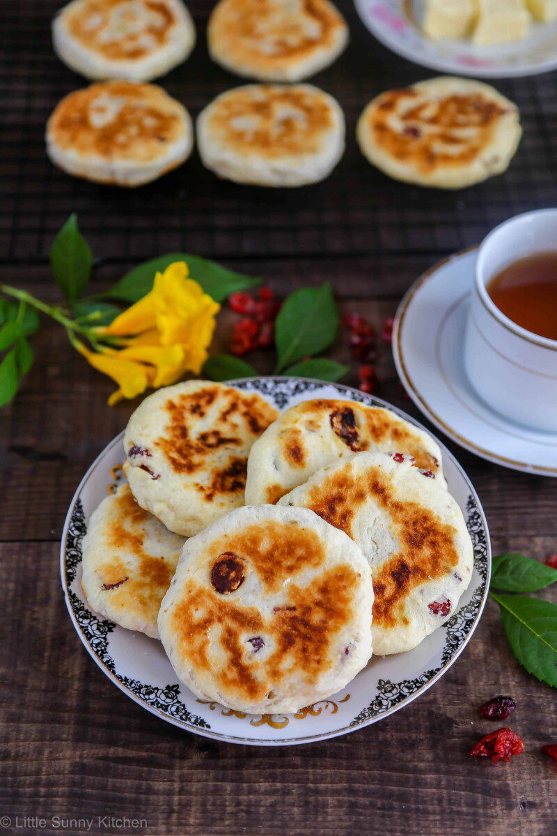 Flat round singing hinnies piled on a patterned plate with a cup of tea