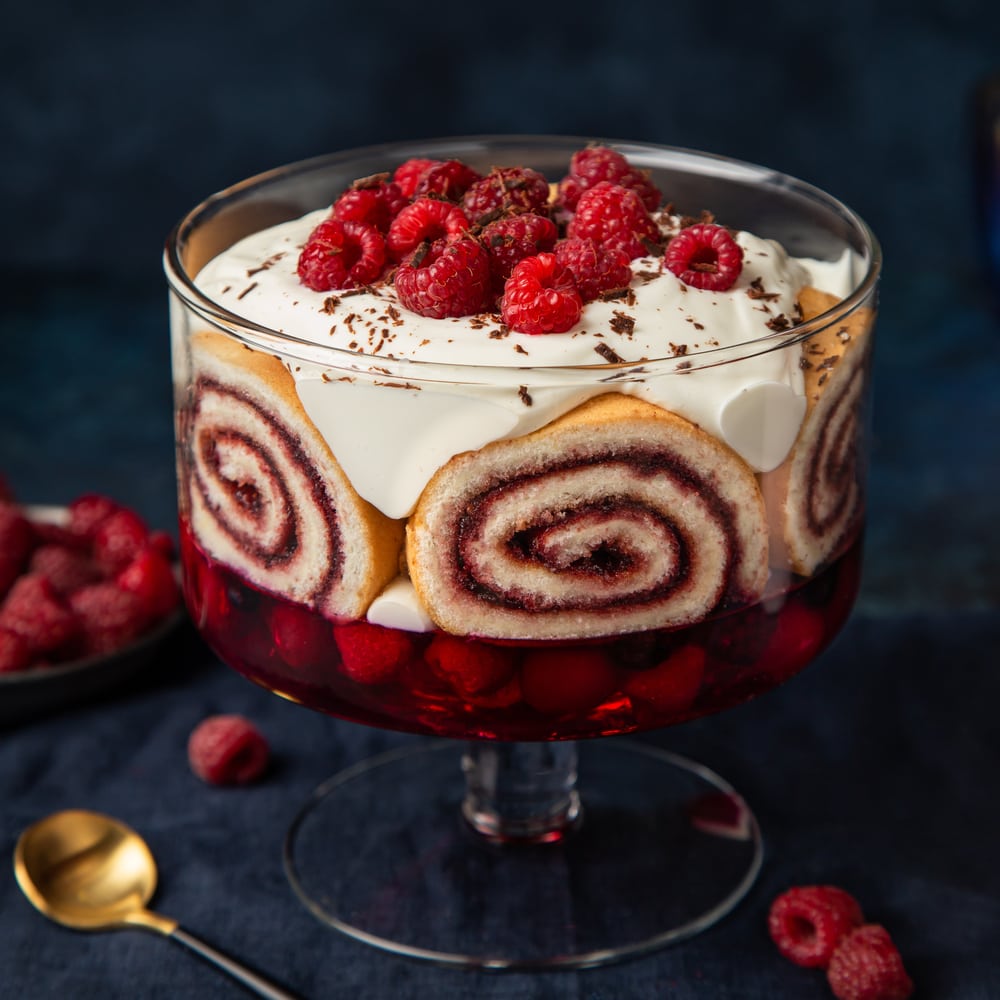 Raspberry trifle with berry jelly, swiss roll cake and whipped cream. Dark blue background,
