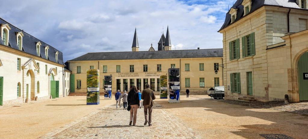 Two people walking down a cobblestone street in front of Fontevraud Royal Abbey.