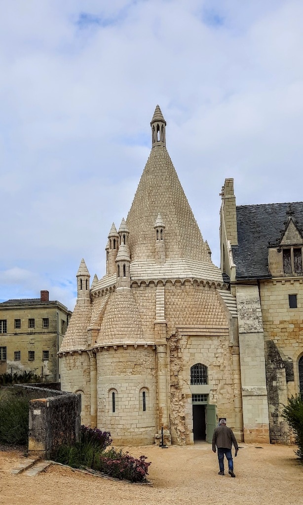 A man walks past the Fontevraud Royal Abbey, a stone building with an ornate roof.