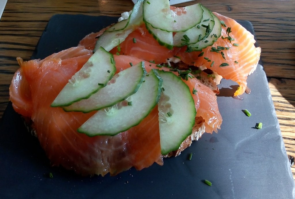 Smoked salmon served on rye bread and topped with chives and cucumber on a black slate dish