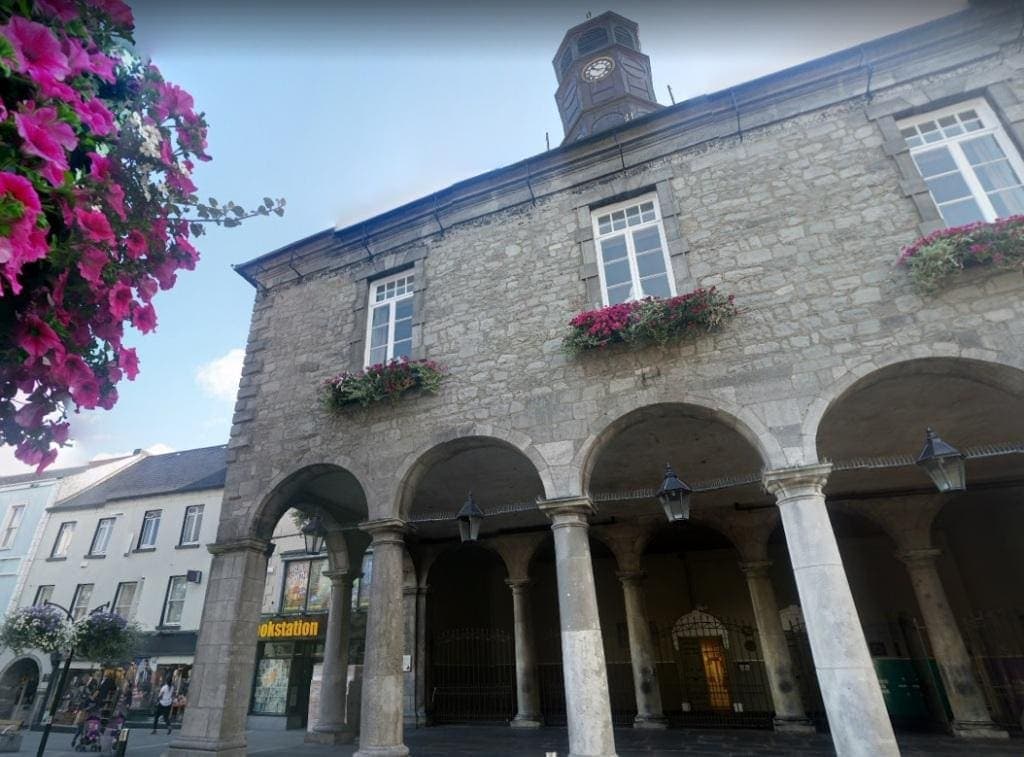 Kilkenny Tholsel City Hall A grey stone building with 4 arches covering an arcade and boxes of pink petunias at the windows above the arches