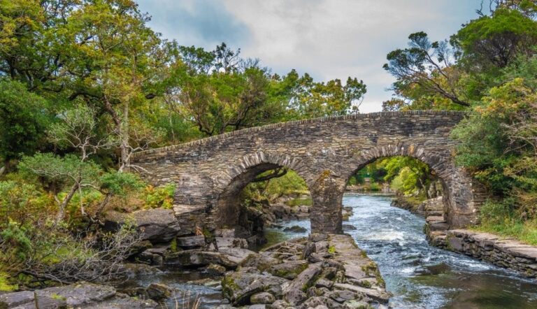 An old Killarney Bridge in Killarney national park. The bridge has two arches and is made of old stones plucked from the land. The river is blue and fast running