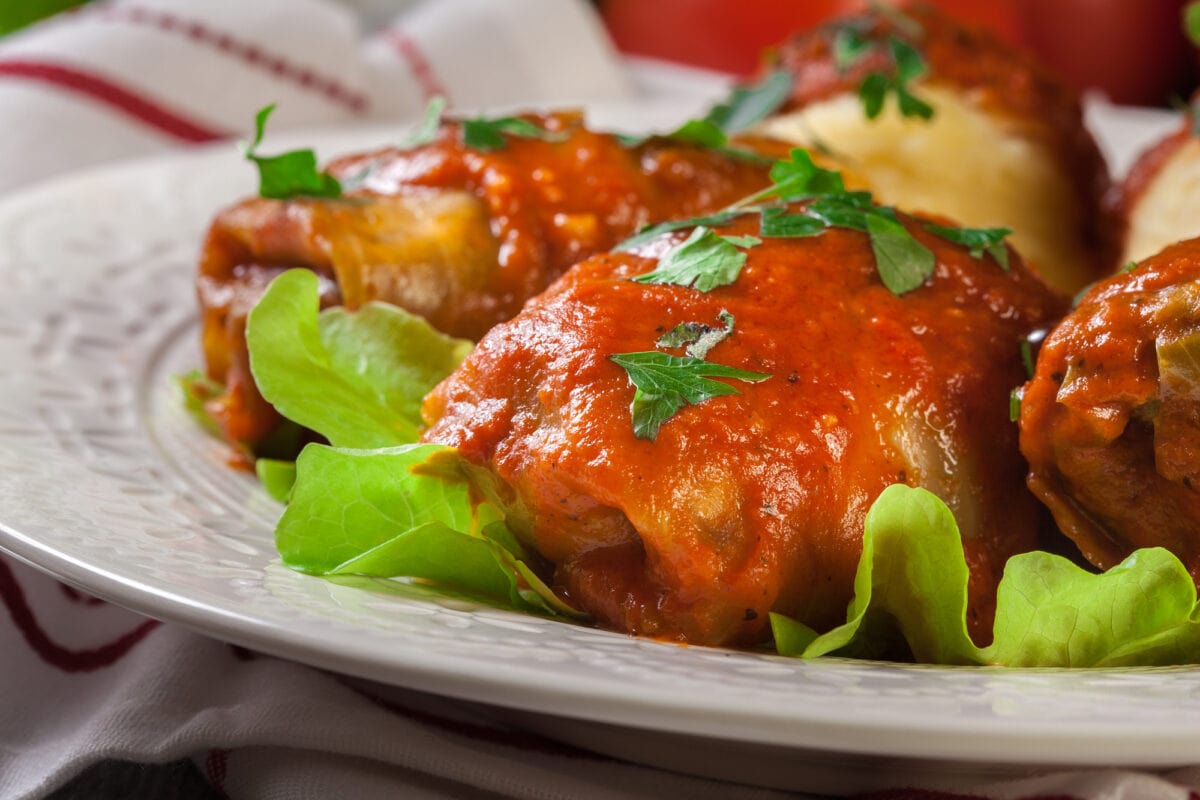 Stuffed cabbage with meat and rice served with boiled potatoes and tomato sauce on white plate