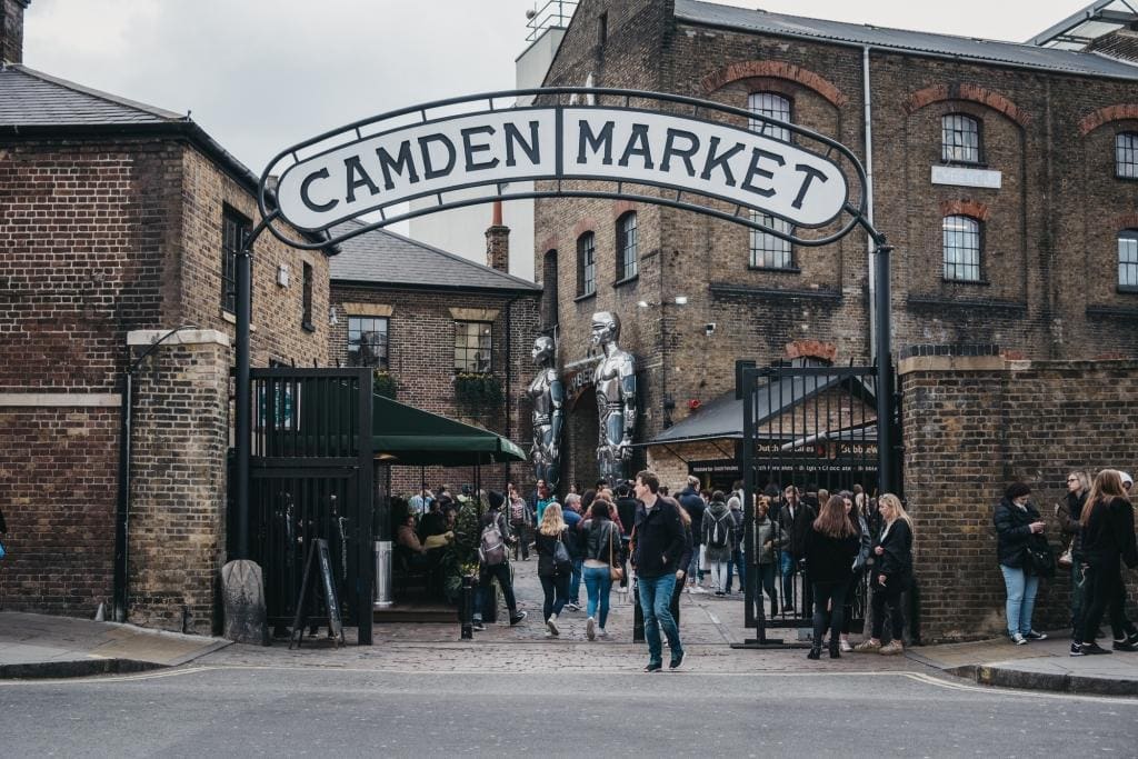 People entering Camden Market, London, UK, through the gates, under a name sign.