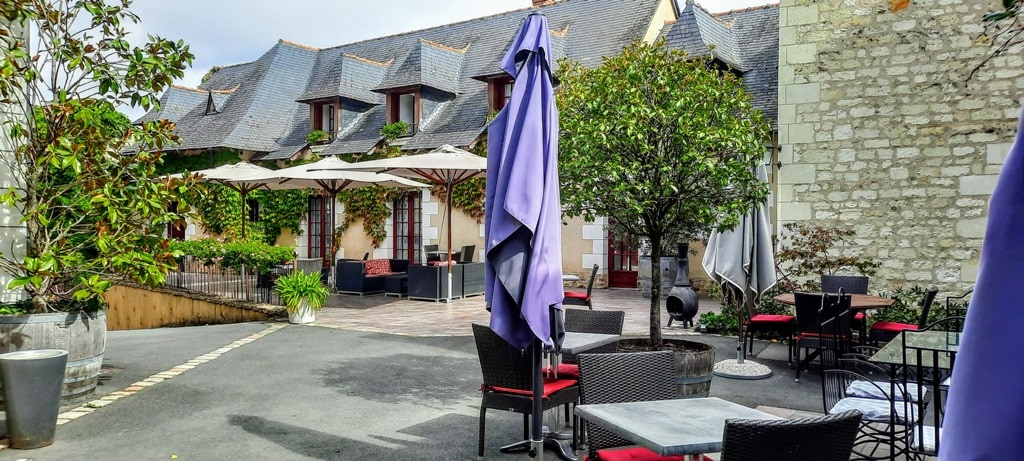 In front of the magnificent Fontevraud Royal Abbey, there is a charming patio area with tables and chairs.