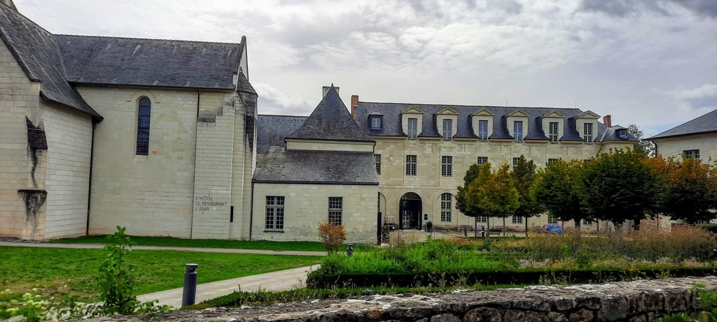 A view of Fontevraud Abbey, a stone building, with a cloudy sky.