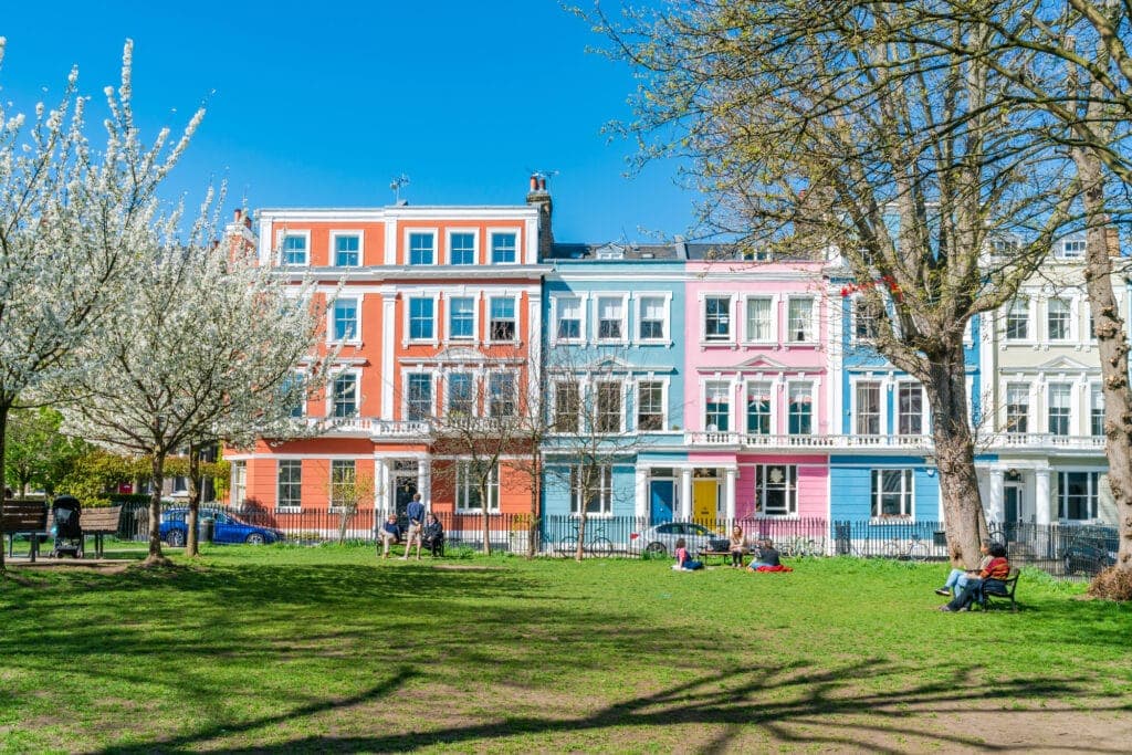 LONDON, UK - MARCH 29 2021: People enjoy sun in Chalcot Square Gardens surrounded by colorful Italianate terraced houses. The Greater London Area of Primrose Hill is often used in films and television