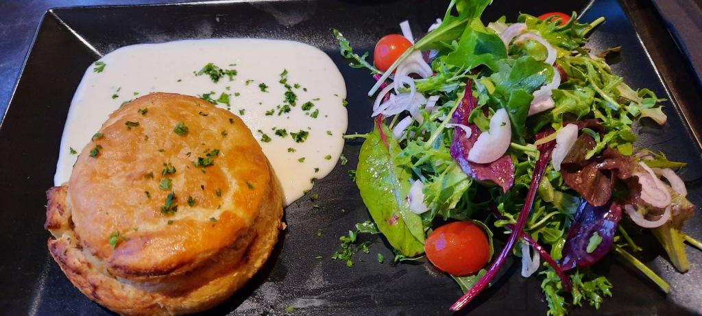 An Anjou starter served at Fontevraud a puff pastry sits on a black plate in a cream sauce with a bright fresh green salad on the side.