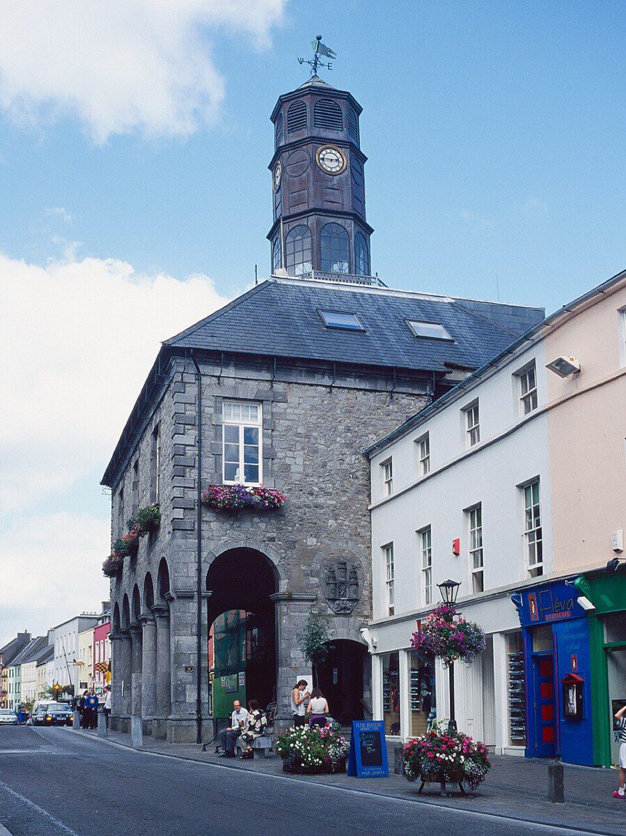 Kilkenny Tholsel City Hall A grey stone building with 4 arches covering an arcade and boxes of pink petunias at the windows above the arches