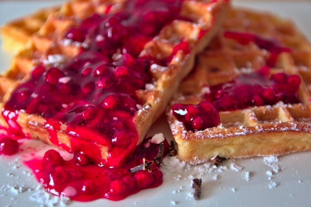 Restaurants in Brussels the national dish of waffles, shown with lots of raspberry jam and powered sugar on a white plate