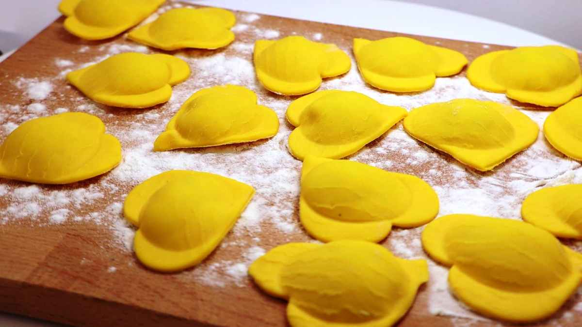 A brown wooden cutting board with bright yellow fresh pasta tortellina in a heart shape