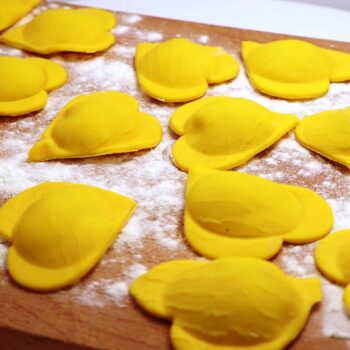 A brown wooden cutting board with bright yellow fresh pasta tortellina in a heart shape