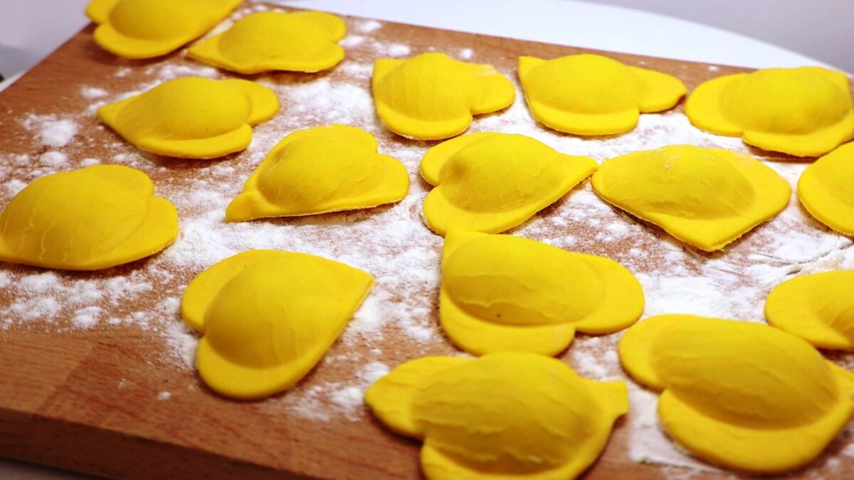 A brown wooden cutting board with bright yellow fresh pasta tortellina in a heart shape