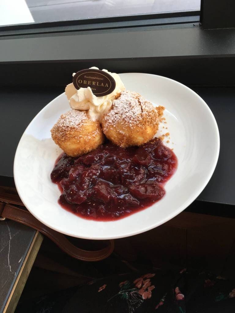 Knoedel served on a white plate with a strawberry jam. The Knoedel are puffs of dough coated with powered sugar