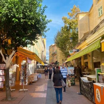 a colourful street market in Menton France with shoppers hurrying back and forth