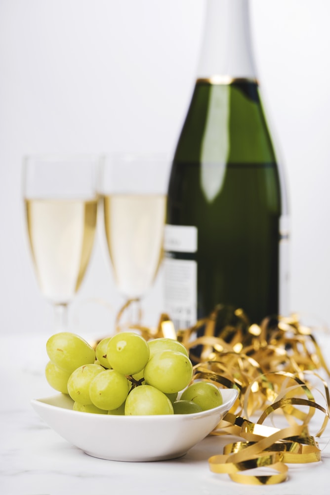 New Year's Eve celebration. Closeup of 12 grapes with a champagne bottle and two glasses blurred in the background on a marble table. 