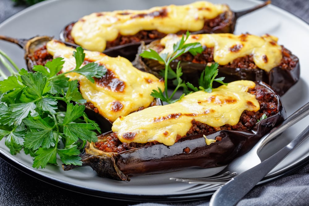 Greek stuffed eggplants with ground beef, tomatoes, topped with bechamel sauce with cheese, served on a plate with parsley on dark concrete background, top view, close-up