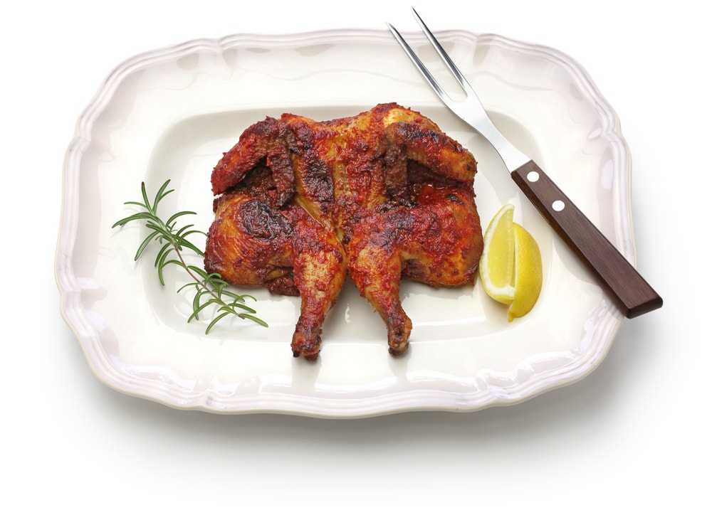 Piri piri chicken a Portuguese traditional dish a chicken spatchcocked on a white plate coated with a chili sauce