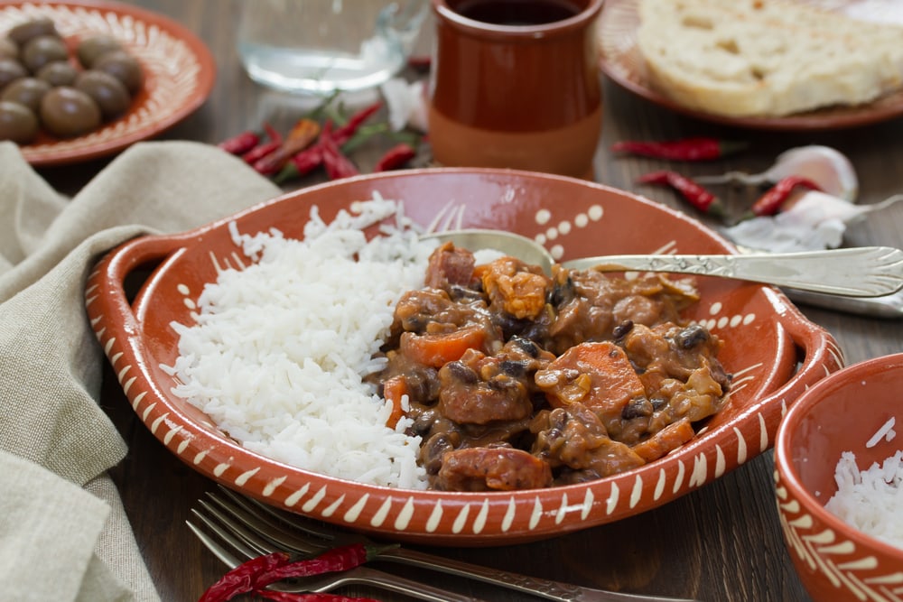 typical portuguese dish feijoada with rice in ceramic bowl and red wine on brown background