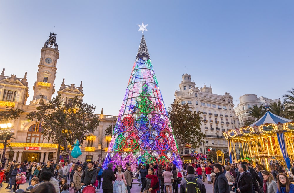 Valencia, Spain - Dec 16, 2017: People having fun on Christmas fair with colorful christmas tree and carousel on Modernisme plaza of the city hall on 16th of December, 2017 in Valencia, Spain.