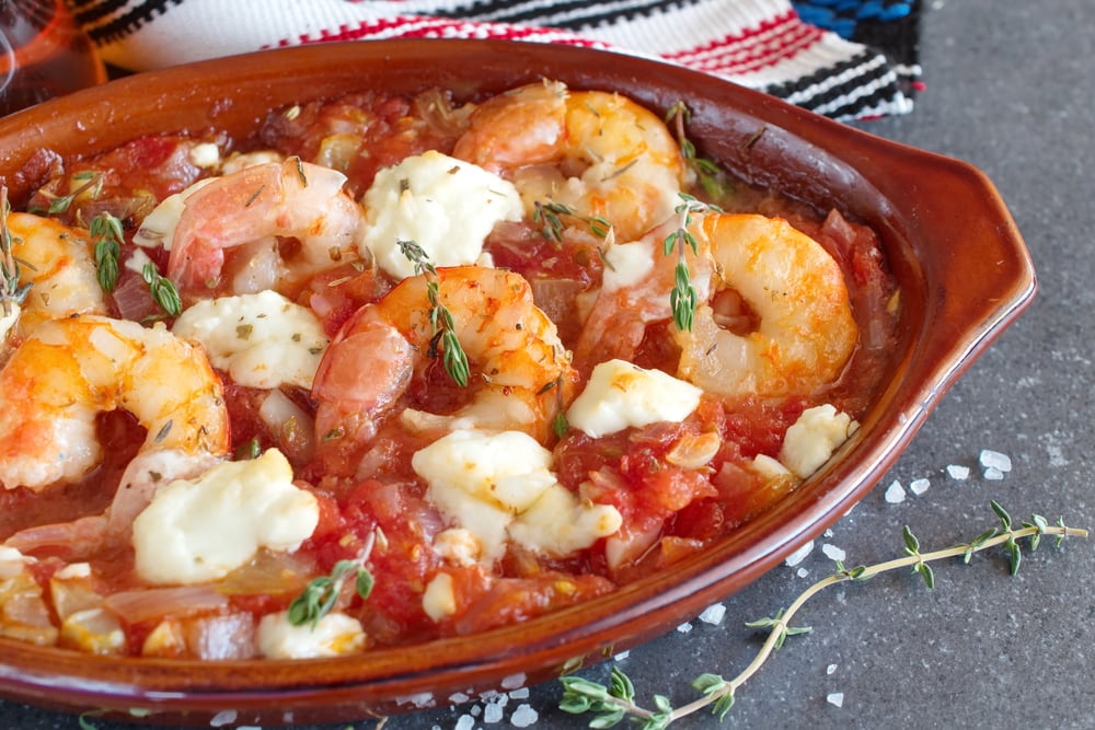 Greek traditional food. Oven backed prawns with feta, tomato, paprika, thyme in a traditional ceramic form on a abstract background. Healthy eating concept. Mediterranian lifestyle.