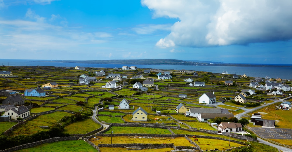 Panoramic landscape of Inisheer Island, part of Aran Islands, Connemara Ireland. Low stone walls separate small white and cream houses near the Atlantic waters of the island.