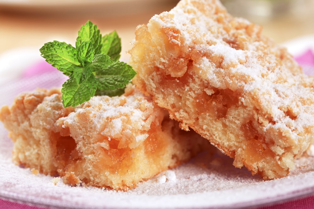 Slices of apple cake with crumb topping on a white plate dusted with icing sugar