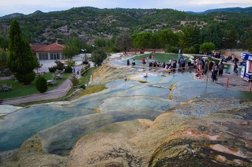 Karahayit, Pamukkale / Denizli, Turkey - September, 2018: Clear warm water in red travertine terraces. Hot springs terraces view. Turkish tourist people bathing and drinking thermal water for health.