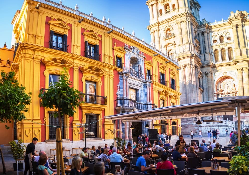 Plaza del Obispo of Malaga surrounded by colourful god and red buildings and a stunning cathedral the crowds in the square are enjoying all tapa and drinks sheltered by a large canopy