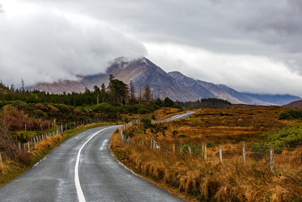 Journey on wild atlantic way in Connemara in Ireland the Sky Road weaves through the brown and green grasses on each verge and the mountains rise up in the distance covered in clouds.